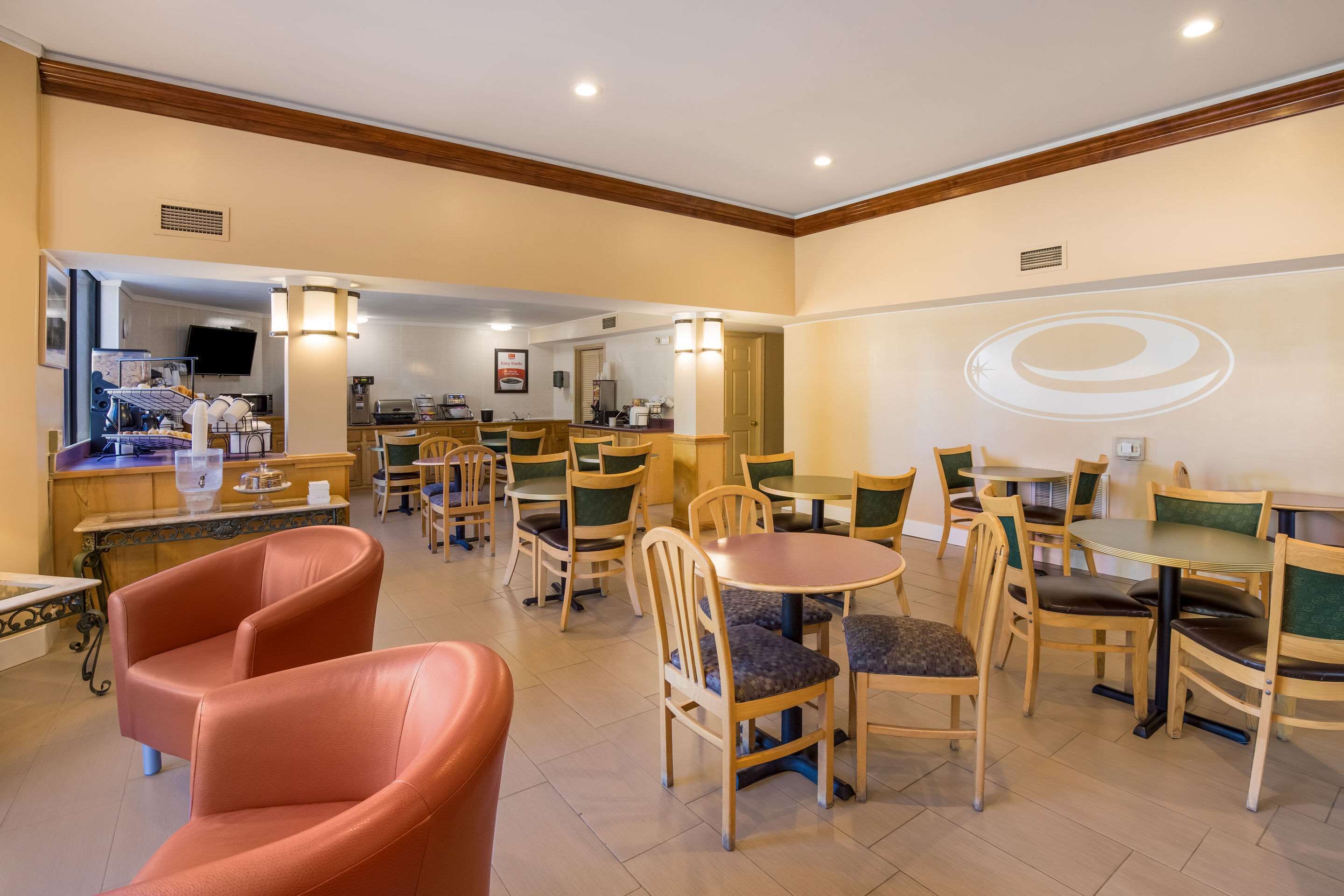 Un comedor de hotel con varias mesas y sillas, una cocina al fondo y una gran decoración en la pared.