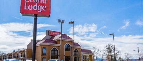 Un hotel llamado Econo Lodge con un letrero rojo, un estacionamiento con varios coches y un cielo azul despejado.