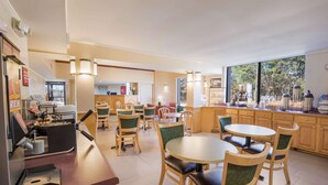 Un restaurant avec des chaises et des tables en bois, un appareil à café et une vue sur l’extérieur grâce à de grandes fenêtres.