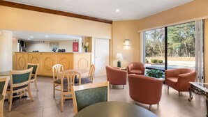 Un hall d’hôtel avec un comptoir d’accueil, des chaises en bois, une table ronde et de grandes fenêtres donnant sur l’extérieur.