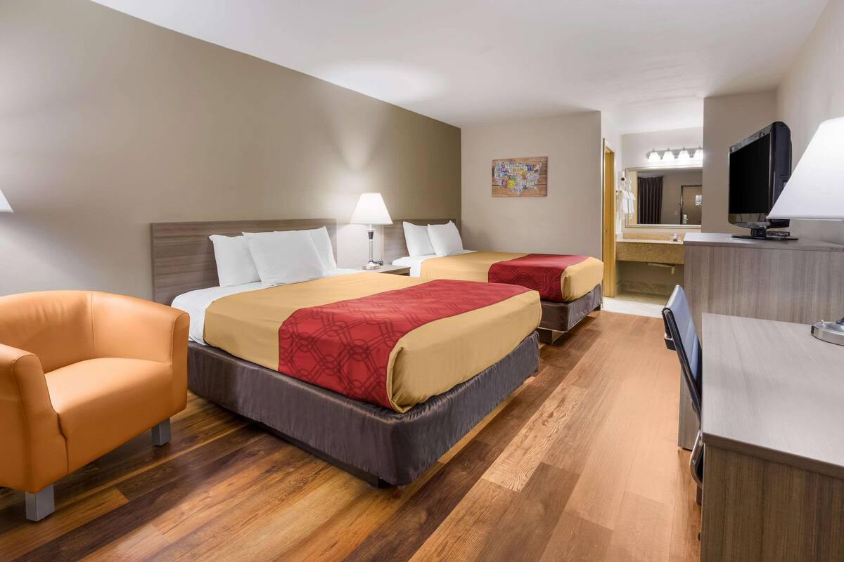 A hotel room with two beds, a sofa, a desk, a TV, and a bathroom mirror.