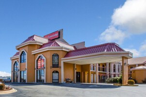 Un hotel con un letrero rojo que dice "Econo Lodge". Cuenta con un estacionamiento techado y una entrada principal con toldo.