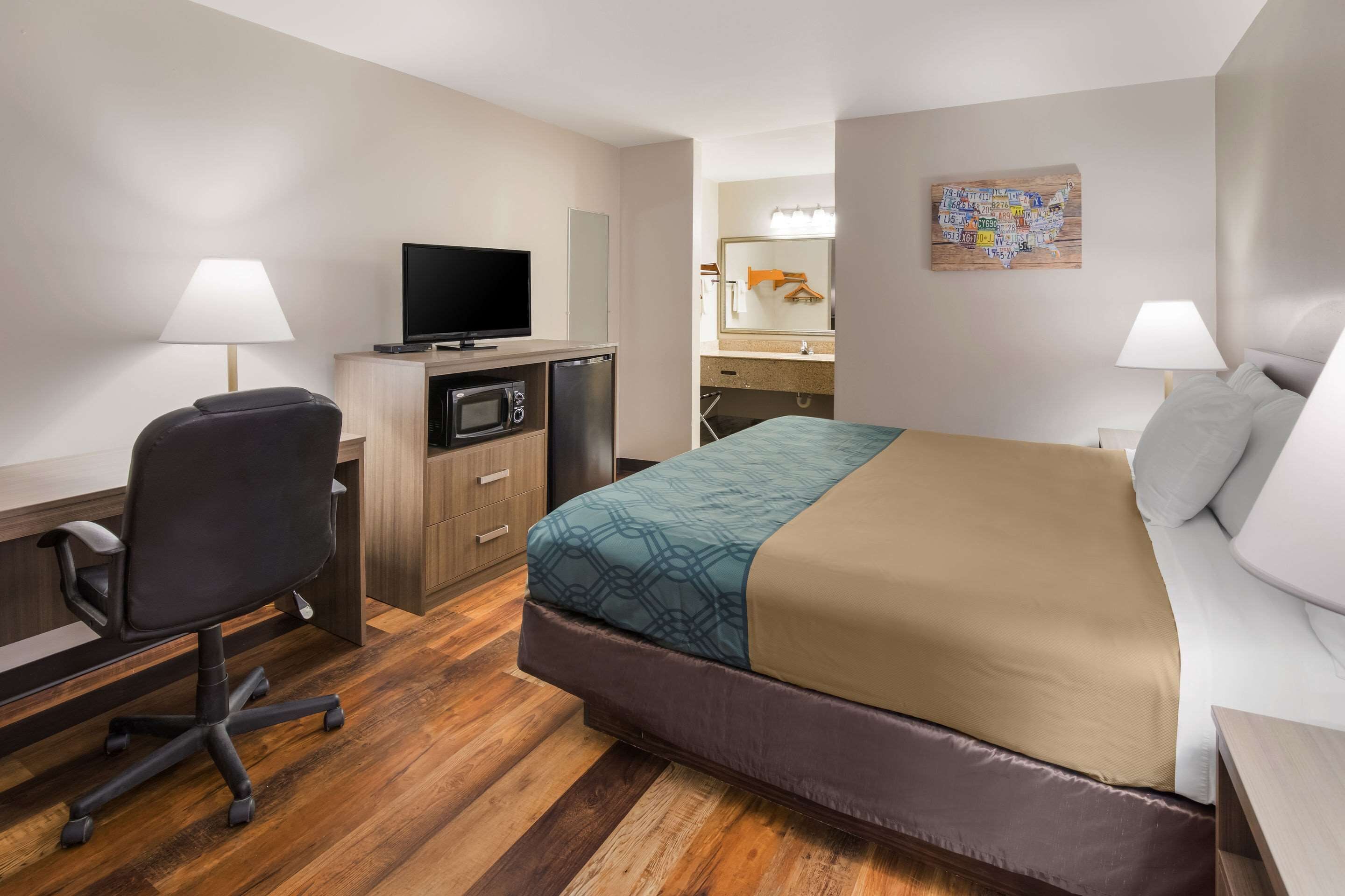 A hotel room with a bed, desk, chair, TV, microwave, and a bathroom visible through an open door.