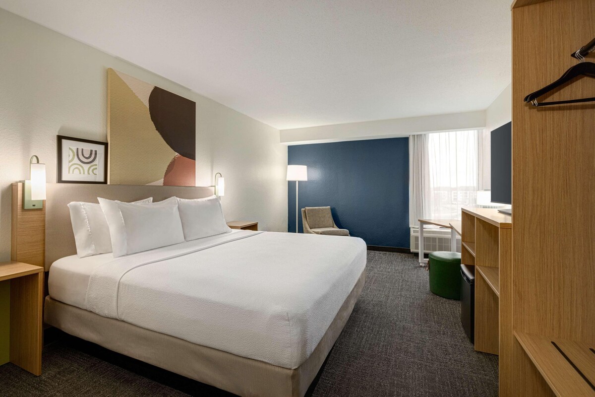A hotel room with a large bed, a desk, a chair, a wardrobe, and a window with curtains.