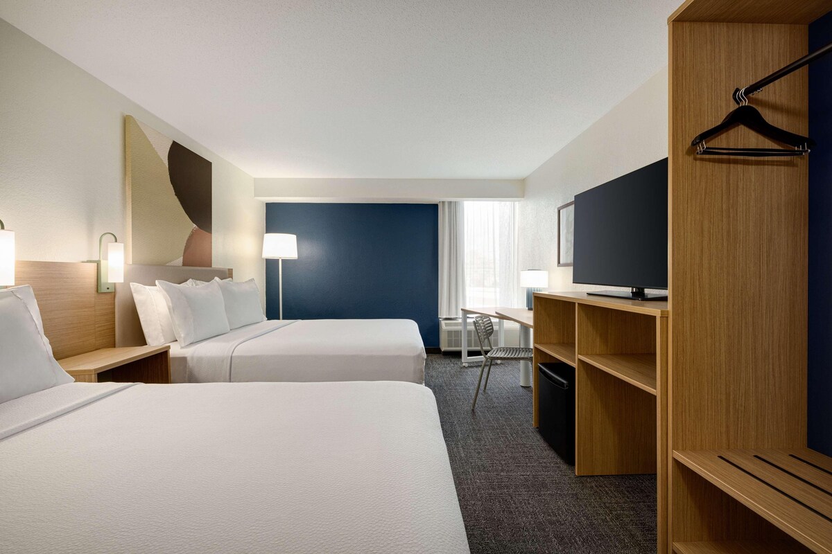 A hotel room with two beds, a desk, a TV, and a wardrobe.