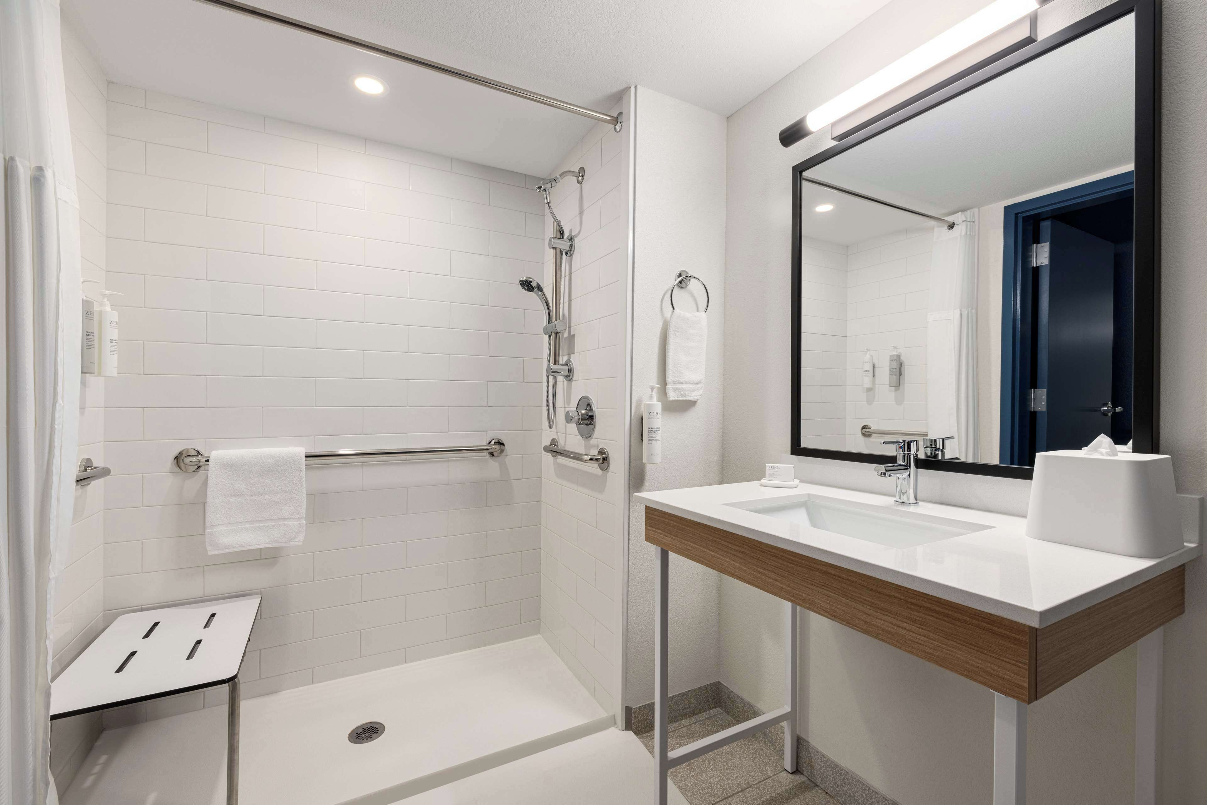 Un baño moderno con ducha a ras de suelo, un lavabo blanco y un espejo grande.