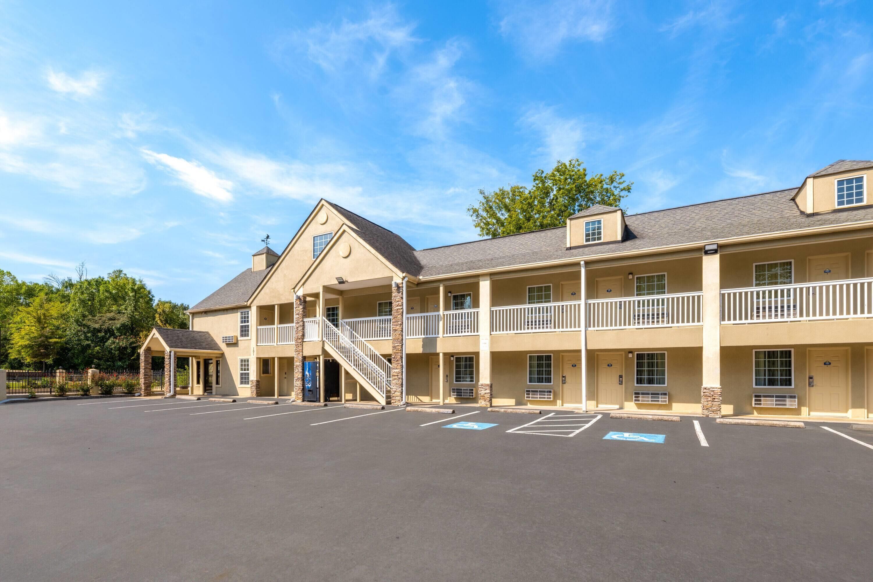 A multi-story motel with a central staircase, balconies, and a parking lot with handicapped parking spaces.