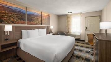 A hotel room with a large bed, a desk, a chair, and a view of a mountainous landscape.