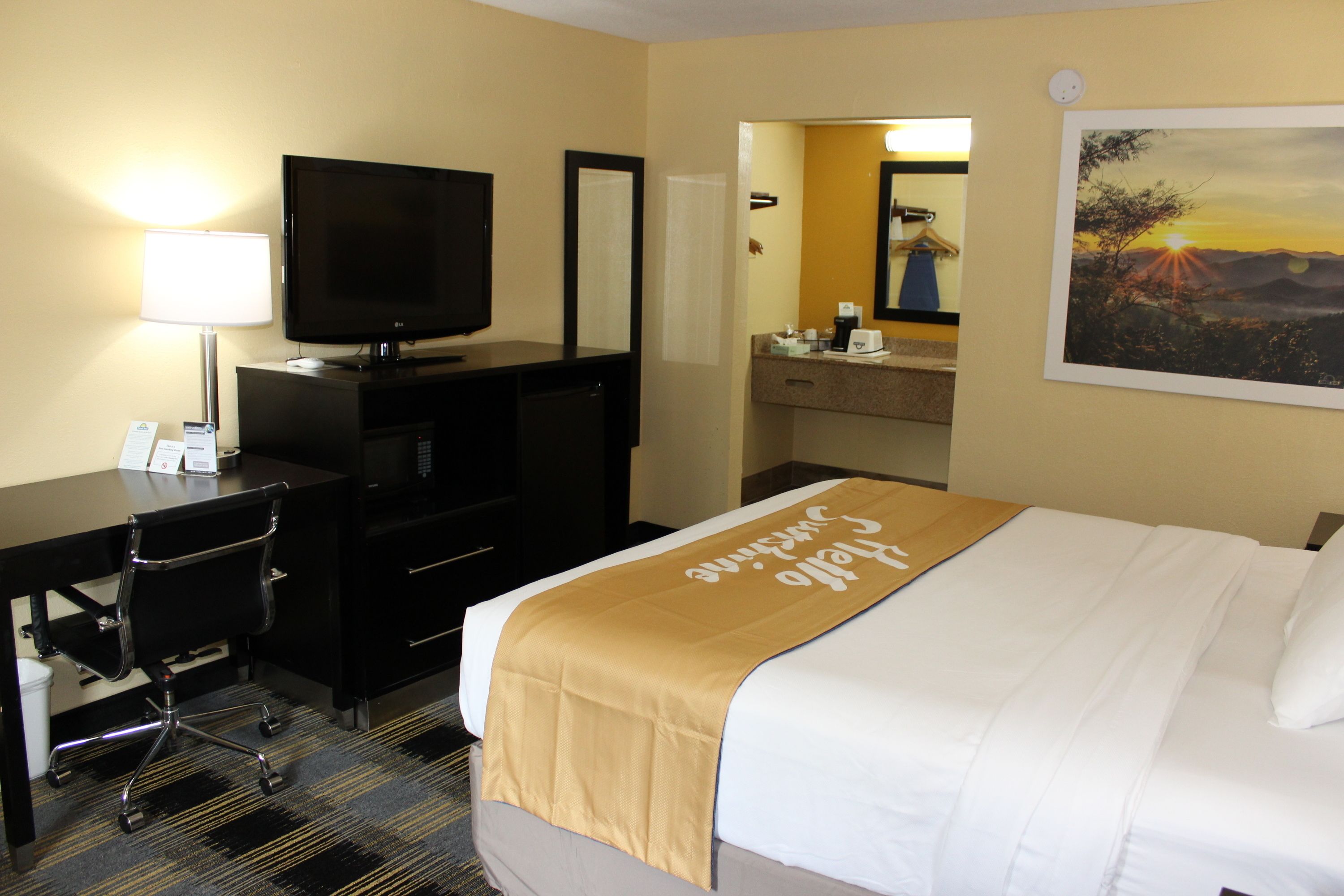 Habitación de hotel con cama, escritorio, televisor, espejo y un cuadro en la pared.