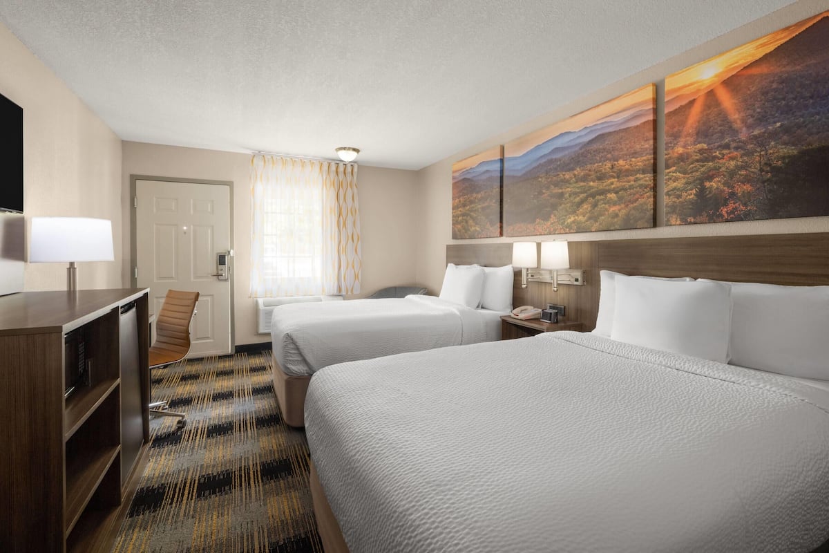 A hotel room with two beds, a desk, a chair, and a large landscape painting on the wall.