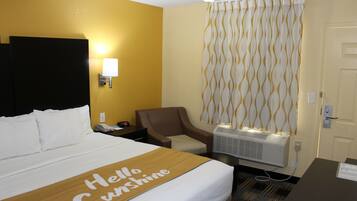 A hotel room with a bed, a chair, a desk, and a wall-mounted air conditioner.