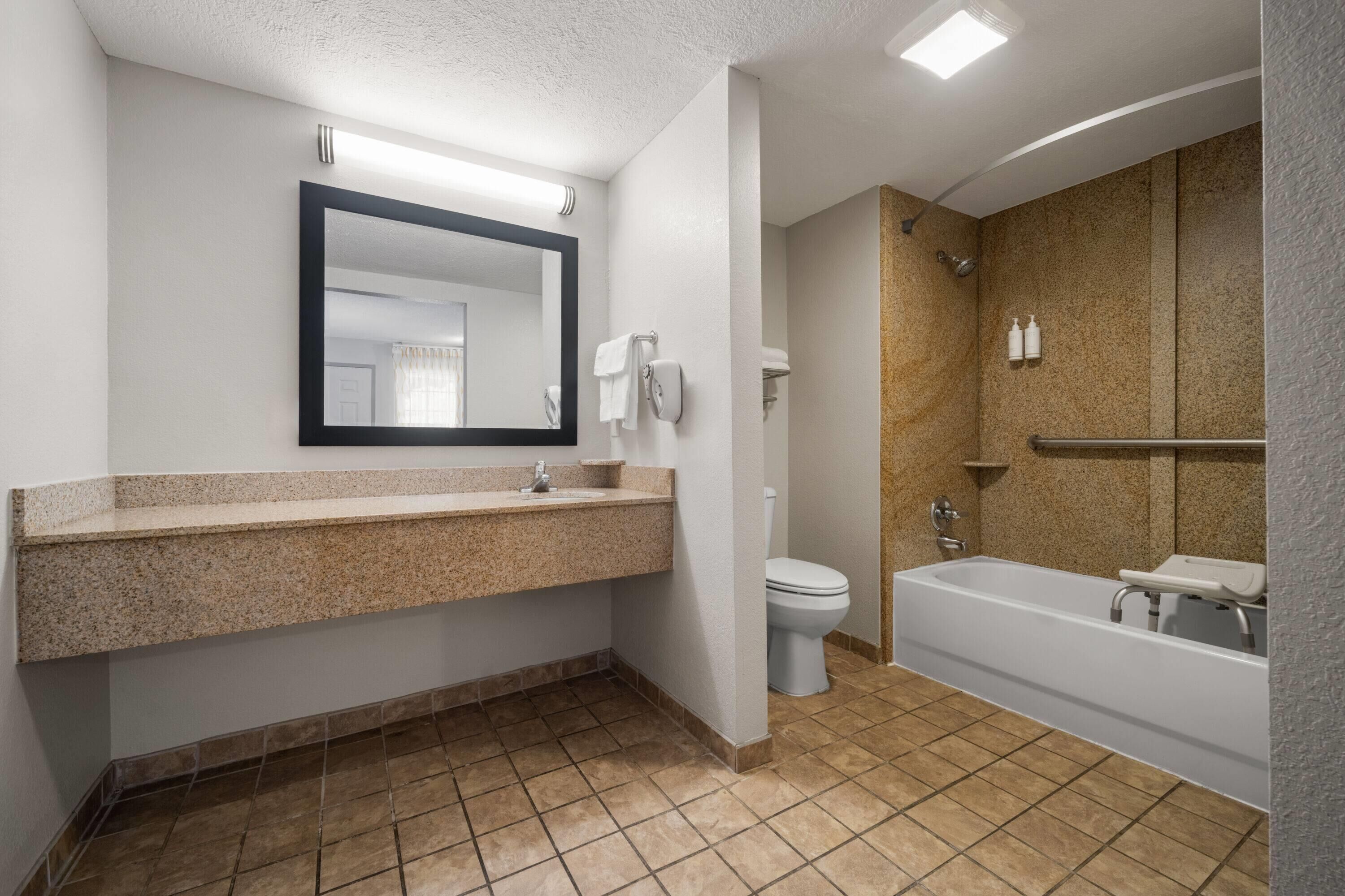 A modern bathroom with a granite countertop, a toilet, and a bathtub.