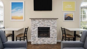A living room with a stone fireplace, two tables, and four chairs. - Days Inn by Wyndham Canton (Canton)