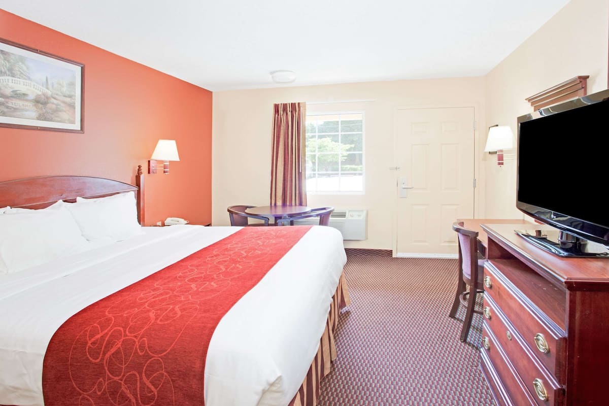 A hotel room with a bed, a television, a desk, and a window with curtains.