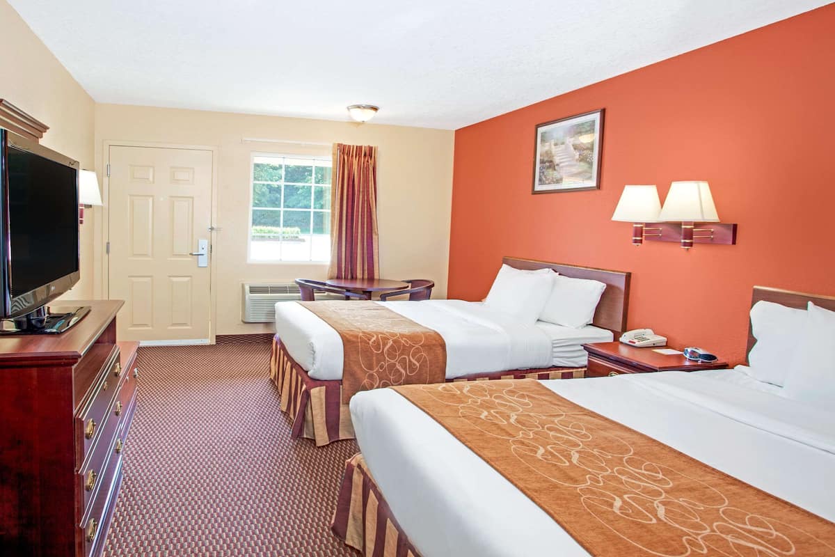 A hotel room with two beds, a TV, a desk, and a window with curtains.