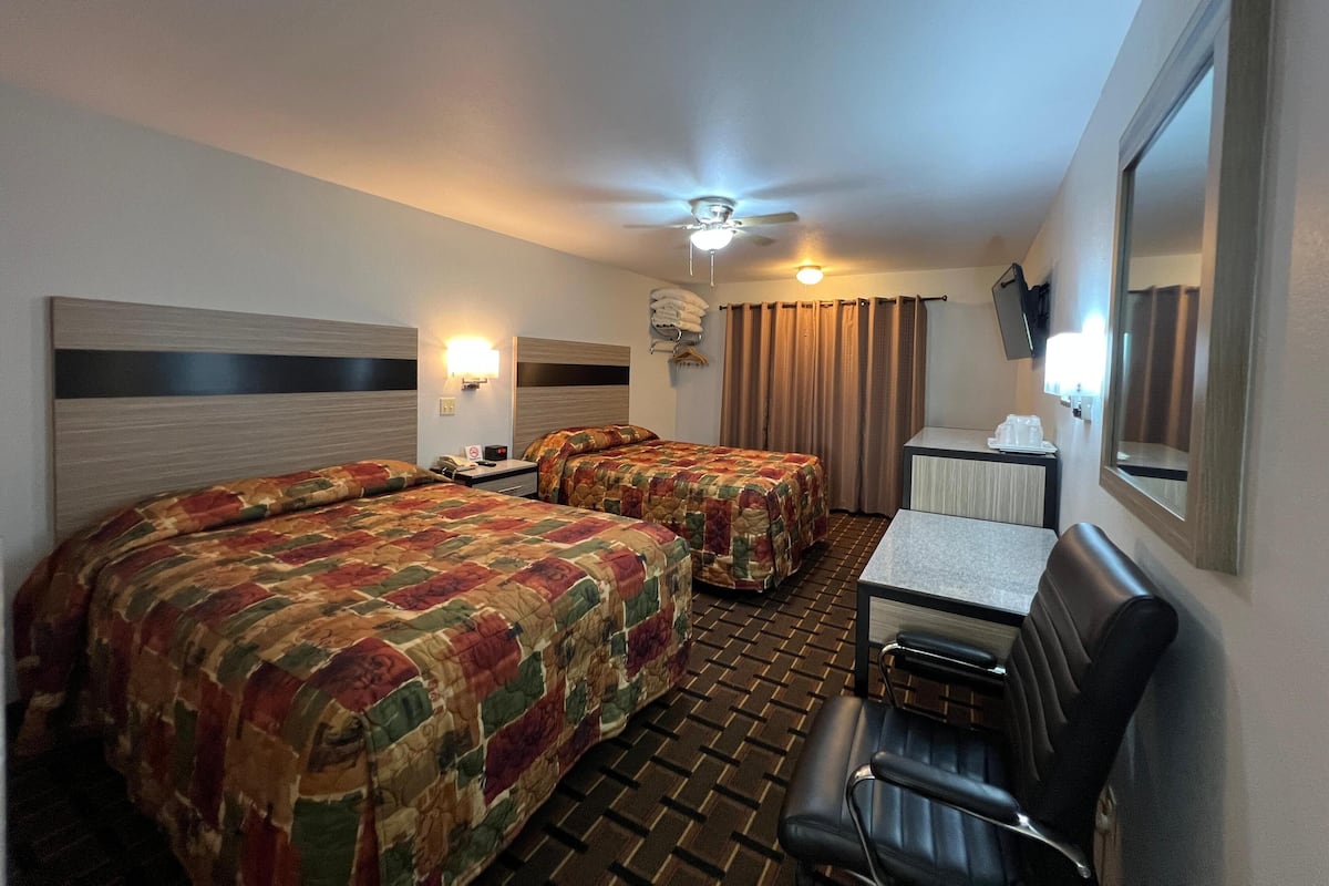 A hotel room with two beds, a desk, a chair, a ceiling fan, and a mirror.