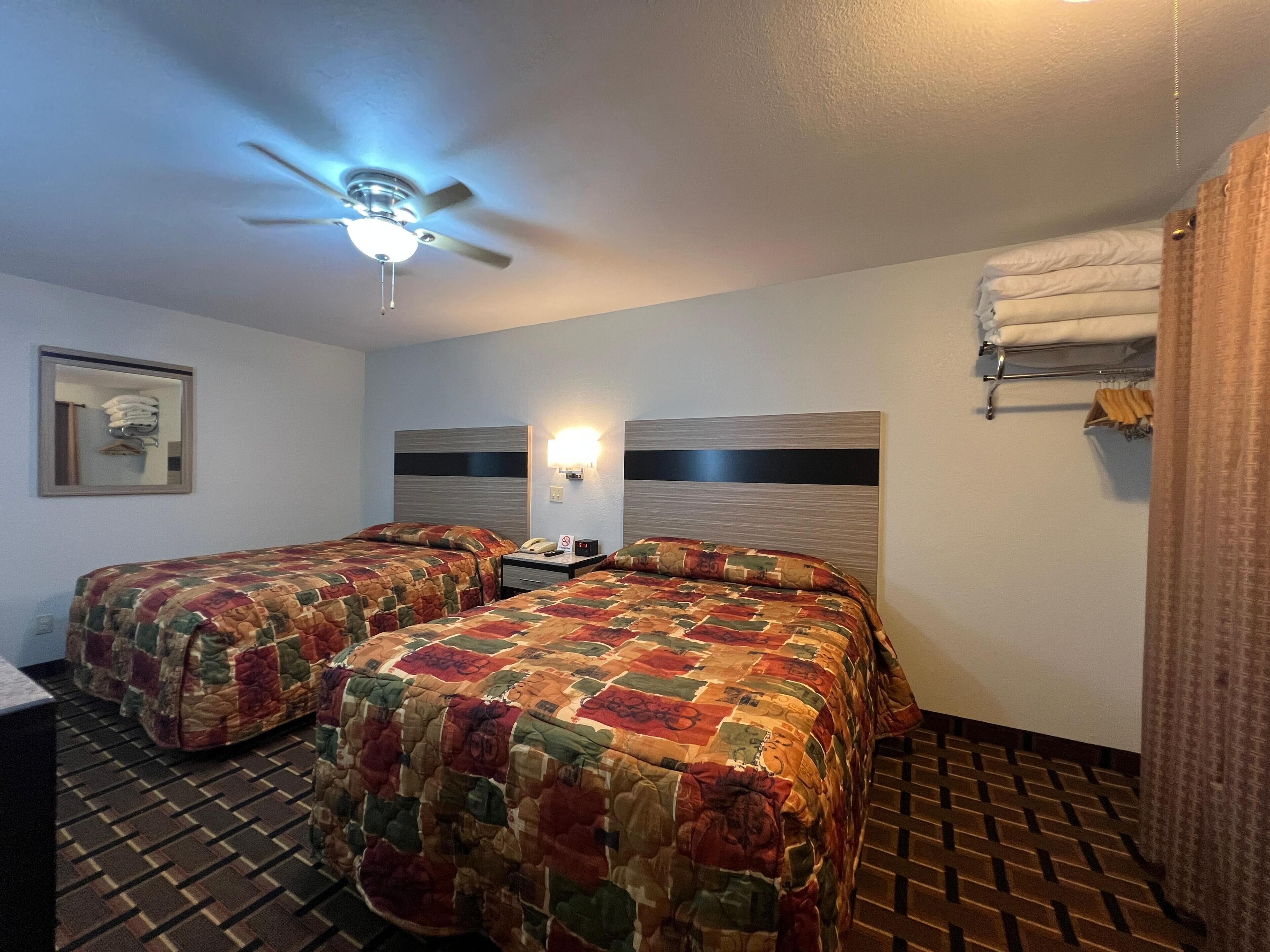 A hotel room with two beds, a ceiling fan, a nightstand, a lamp, and a mirror.