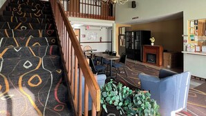 A hotel lobby with a staircase, a chandelier, seating area, and a reception desk.