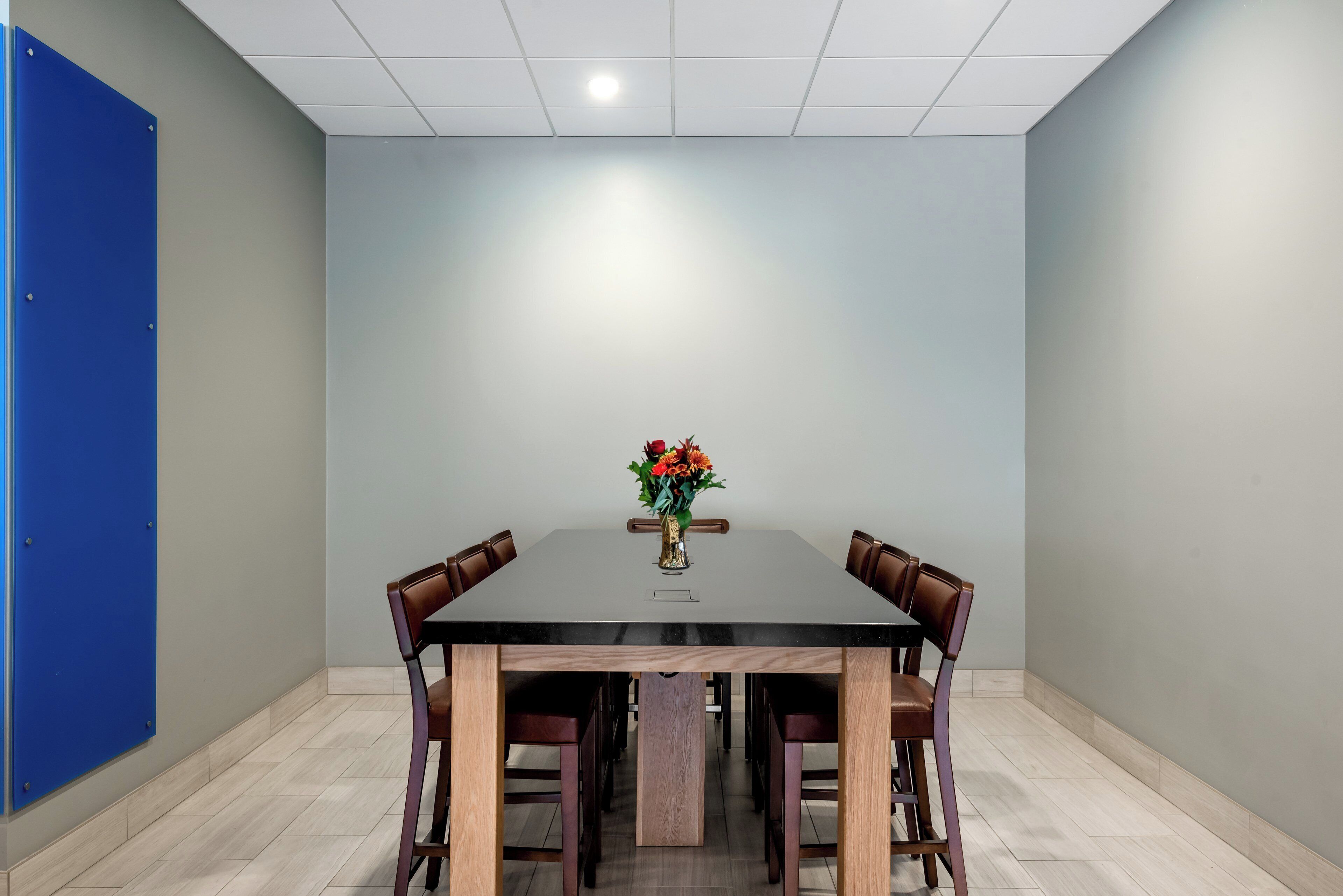 Un salón de conferencias con una mesa rectangular, cuatro sillas y un florero con flores.