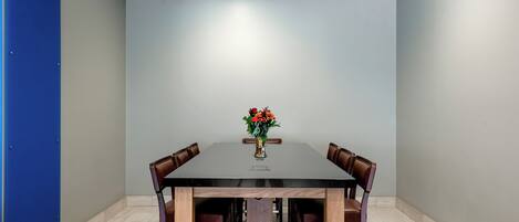 Un salón de conferencias con una mesa rectangular, cuatro sillas y un florero con flores.
