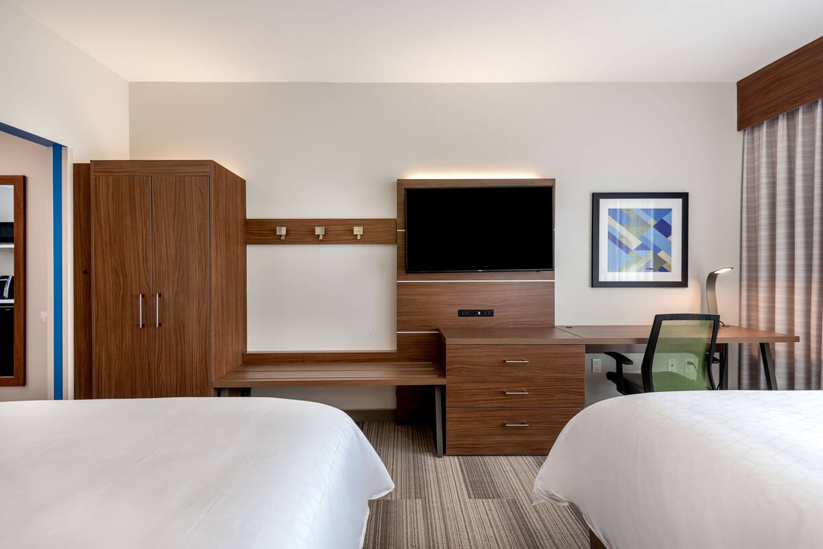 A hotel room with two beds, a desk with a flat-screen TV, a wooden wardrobe, and a framed picture on the wall.
