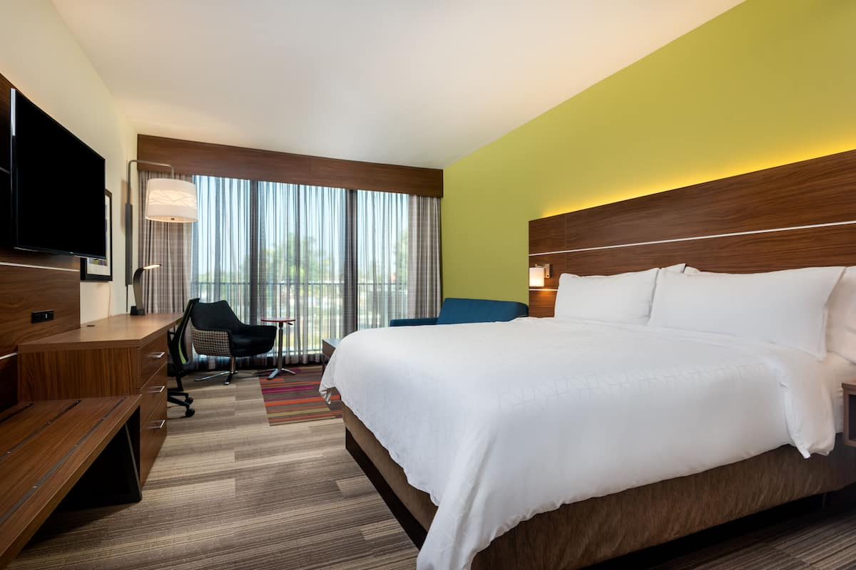 A hotel room with a large bed, a desk with a chair, a TV, and a window with curtains.