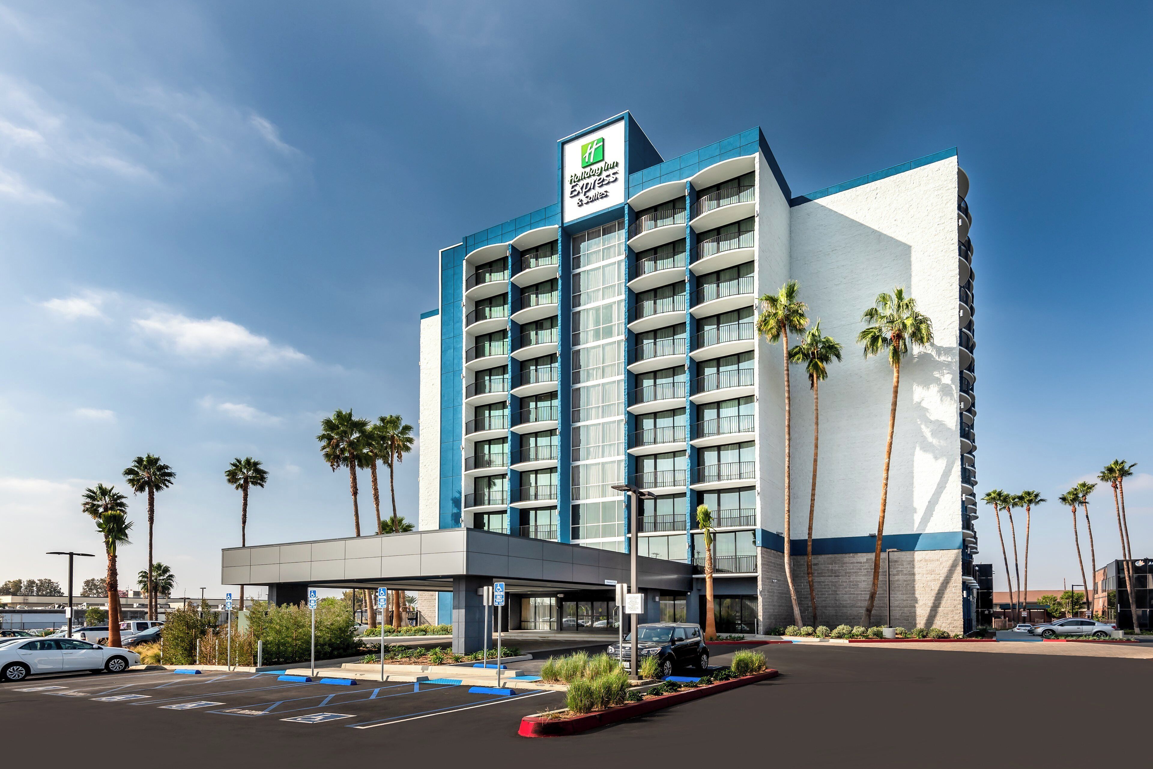 A hotel with a modern design, featuring a prominent entrance, multiple floors, and a parking area with marked spaces.