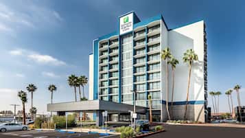 A hotel with a modern design, featuring a prominent entrance, multiple floors, and a parking area with marked spaces.