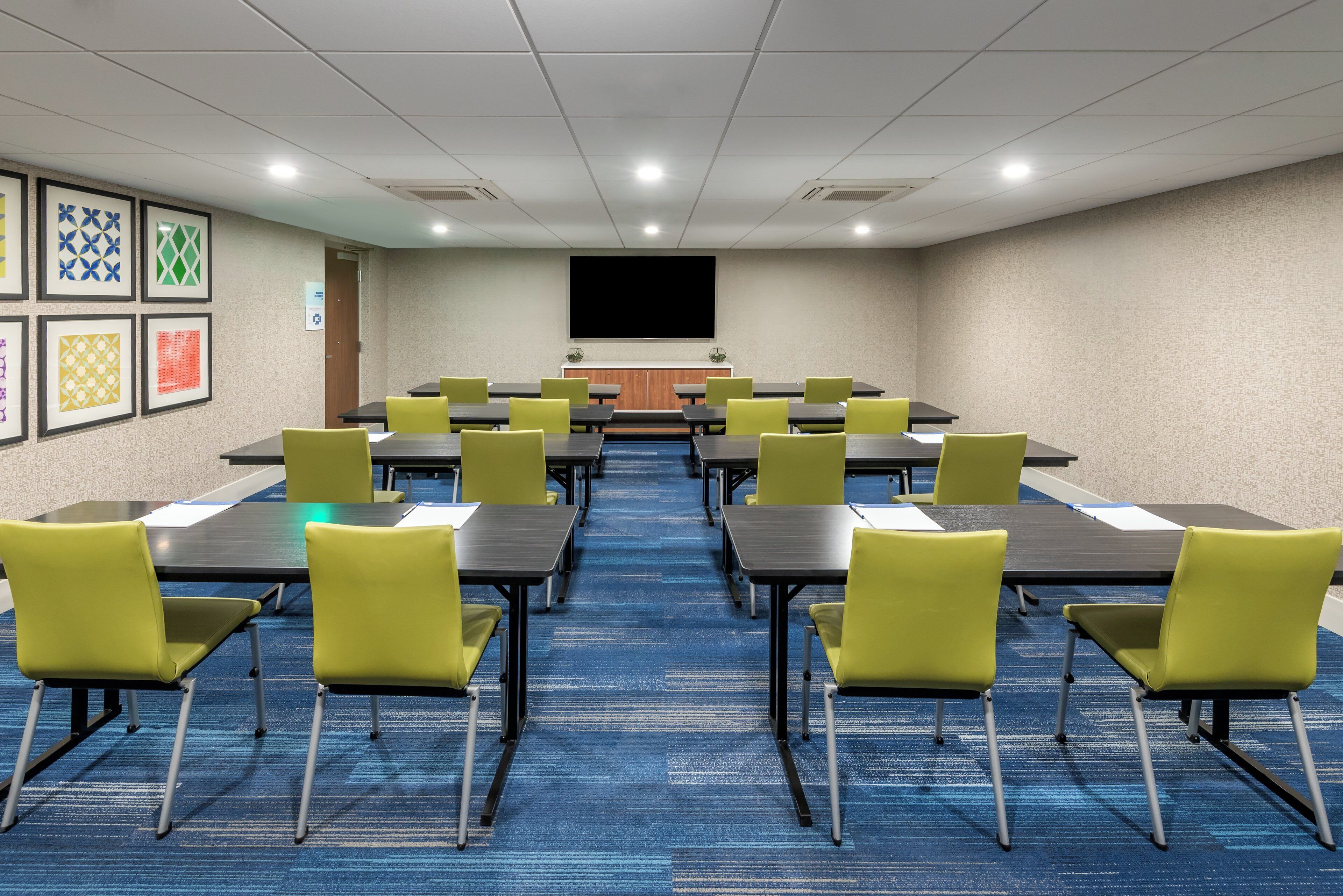 A conference room with tables and chairs, a projector screen, and framed artwork on the walls.