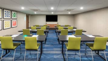 A conference room with tables and chairs, a projector screen, and framed artwork on the walls.