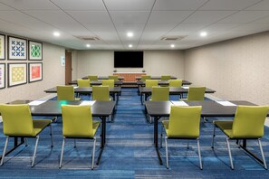 A conference room with tables and chairs, a projector screen, and framed artwork on the walls. - Holiday Inn Express & Suites Santa Ana - Orange County by IHG (Santa Ana)