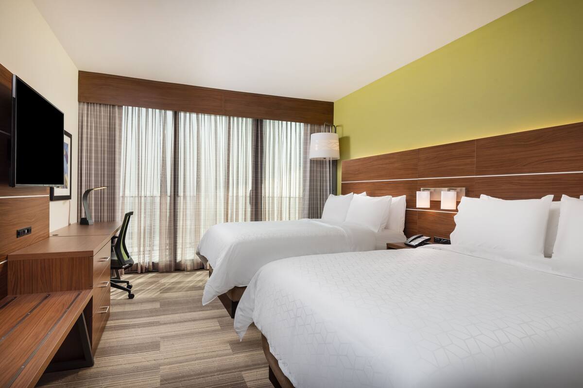A hotel room with two beds, a desk, a chair, and a TV.