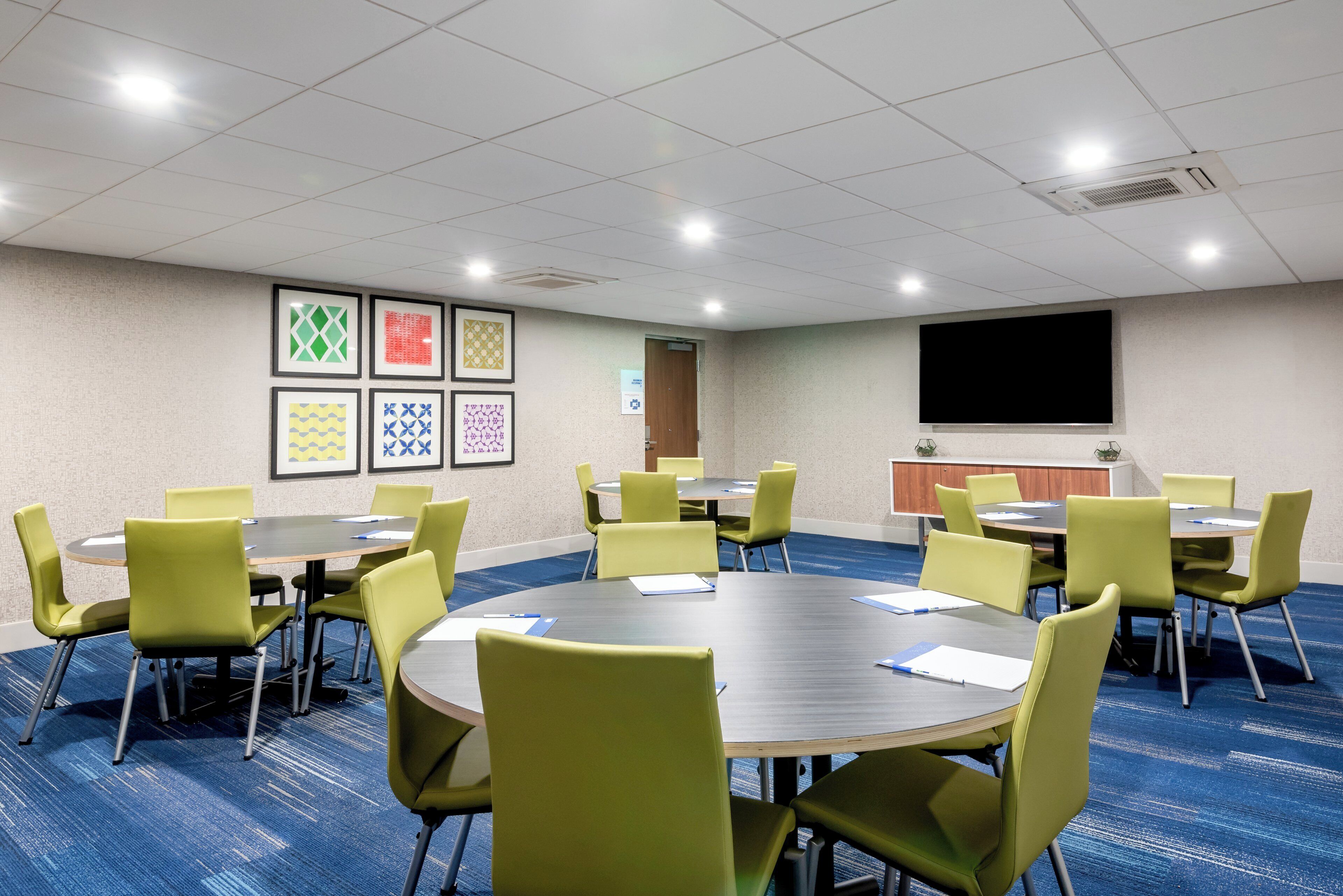 A conference room with round tables, green chairs, and framed artwork on the walls.