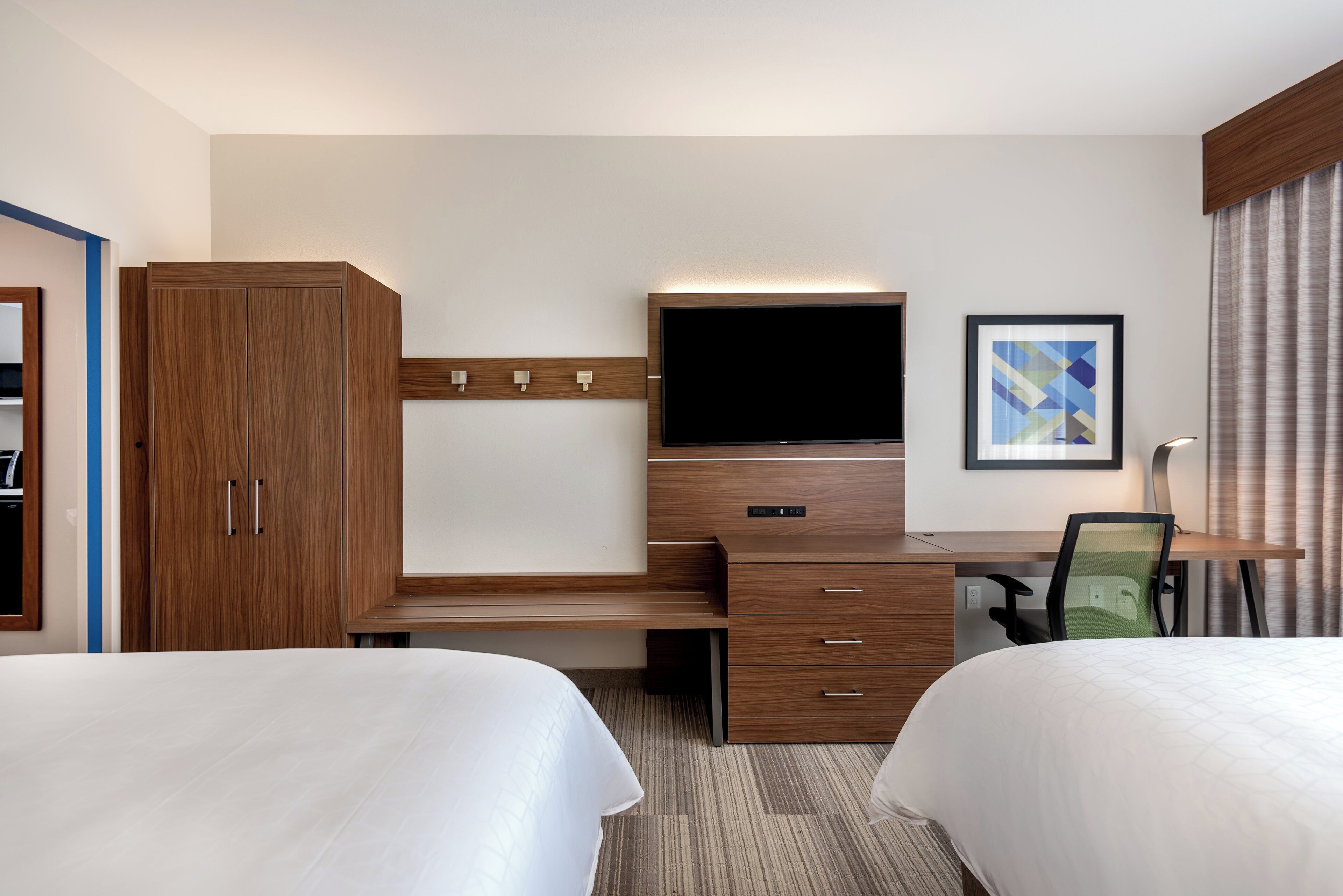 A hotel room with two beds, a desk with a flat-screen TV, a wardrobe, and a framed picture on the wall.