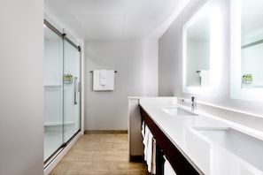 Un baño moderno con ducha de vidrio, lavamanos blanco y un espejo grande.