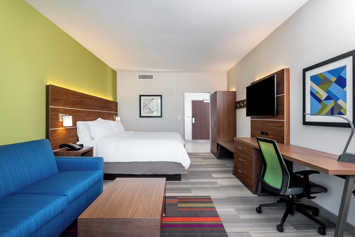 Habitación de hotel con cama, sofá azul, escritorio con silla, televisor y obras de arte en las paredes.