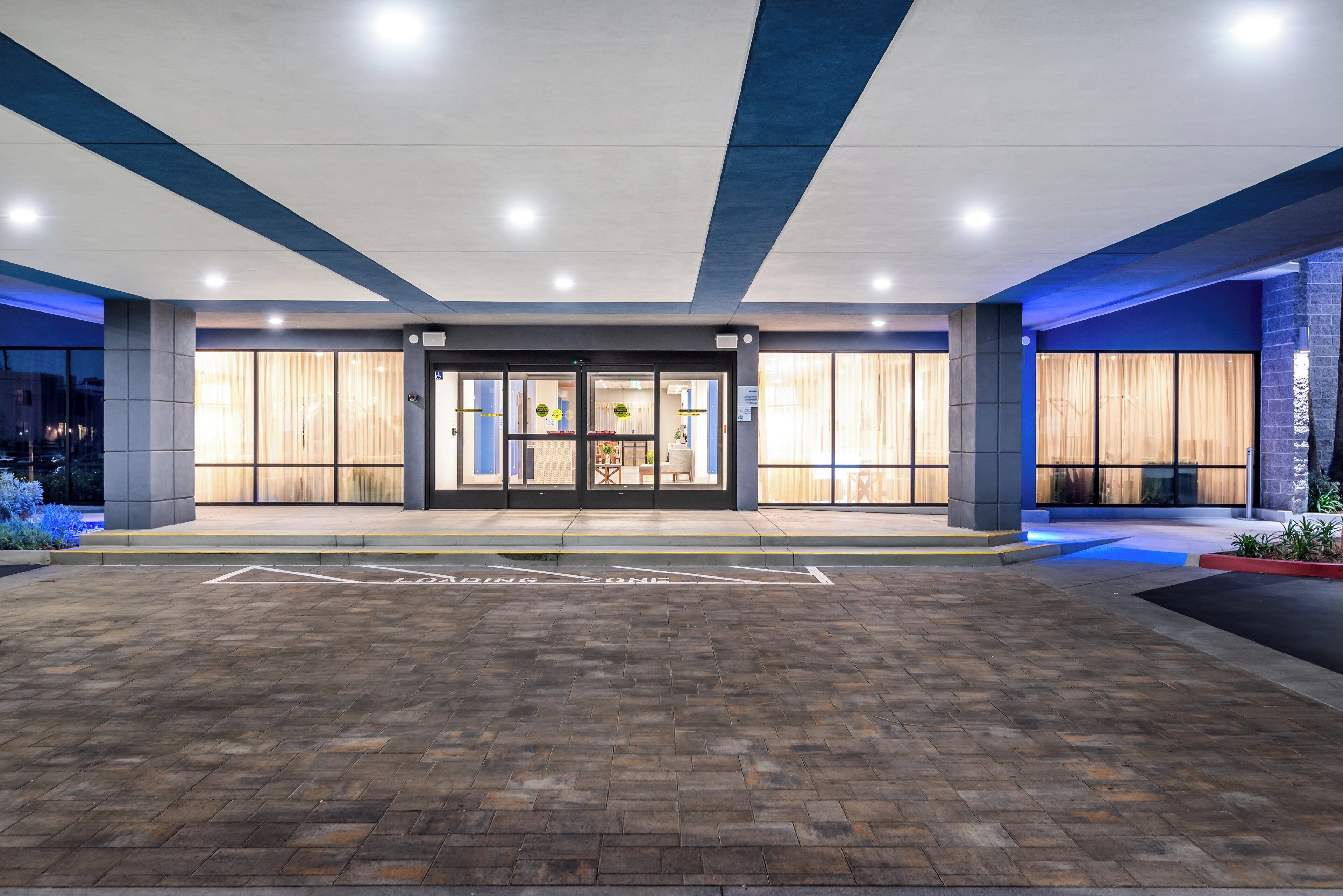 A hotel entrance with a brick-paved driveway, a glass door entrance, and a blue and white color scheme.