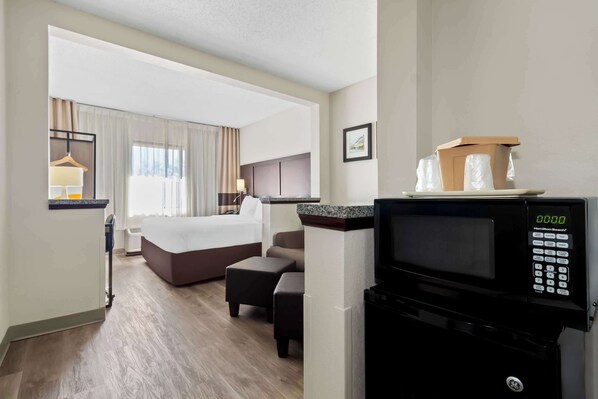 A hotel room with a bed, a seating area, a microwave, and a view of the hallway.