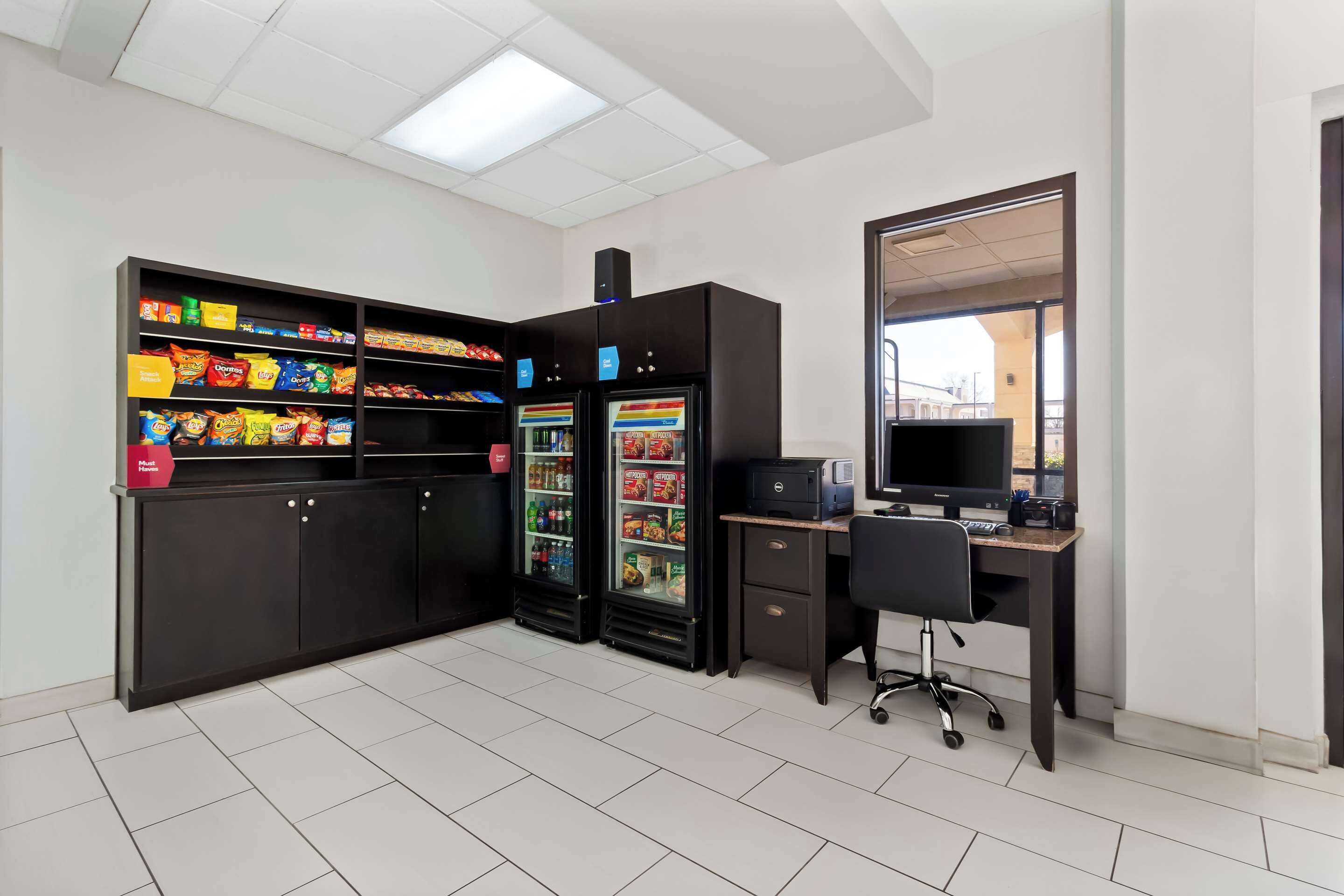 Una habitación con un armario negro, dos dispensadores de bebidas, un escritorio con una computadora y un espejo grande.