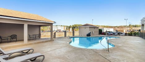 A pool area with lounge chairs and a small building, likely a changing room or utility space, in a resort setting.