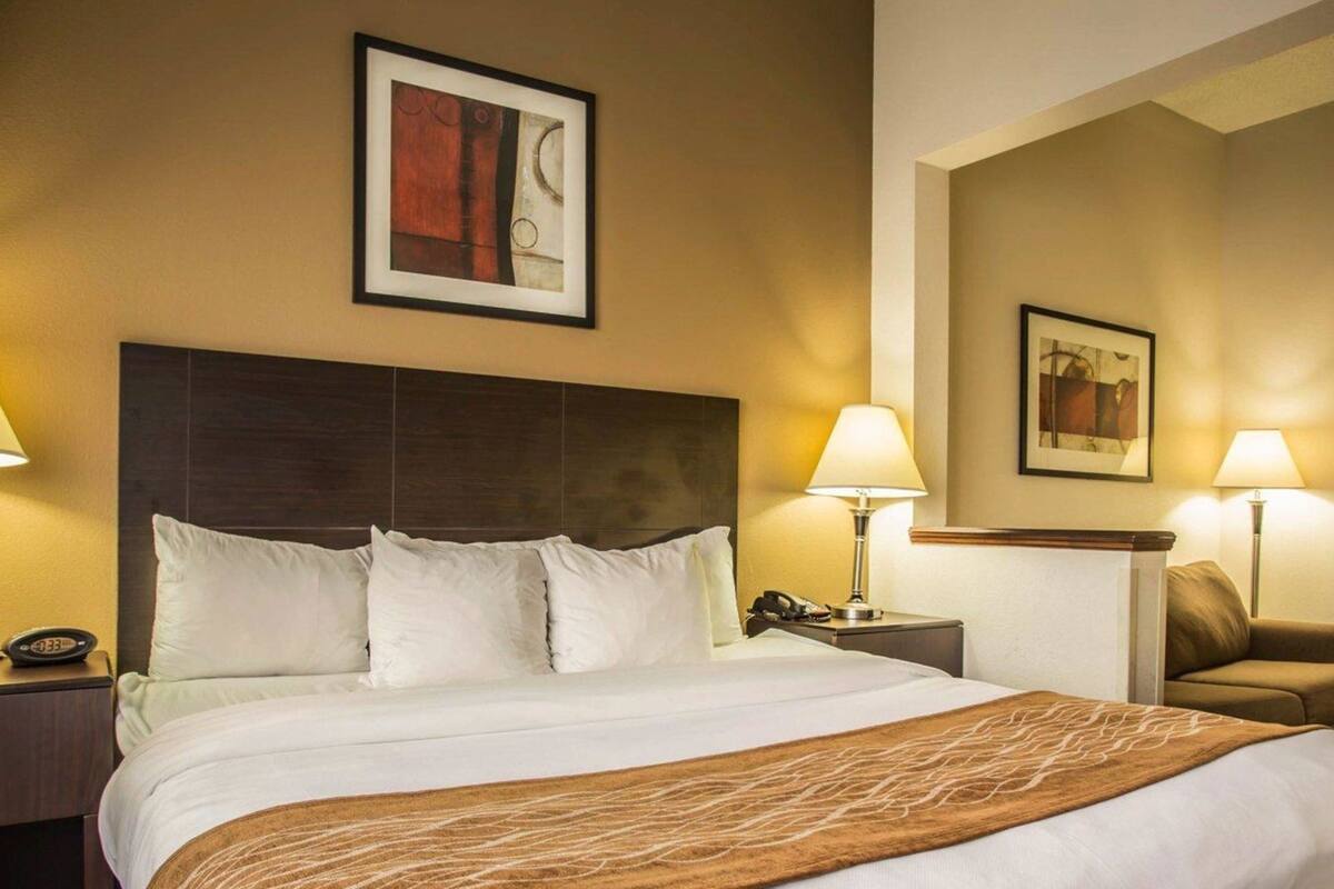 Habitación de hotel con una cama grande, cabecero, dos mesitas de noche con lámparas, una mesita auxiliar y una silla.