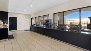 A modern kitchen with a long counter, black cabinets, and a view of a building through large windows. - Comfort Suites Lumberton North (Lumberton)