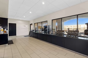 A modern kitchen with a long counter, black cabinets, and a view of a building through large windows. - Comfort Suites Lumberton North (Lumberton)