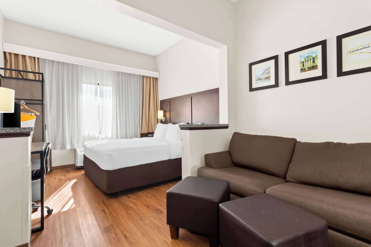 A hotel room with a bed, a sofa, a desk, and a chair. There are three framed pictures on the wall.