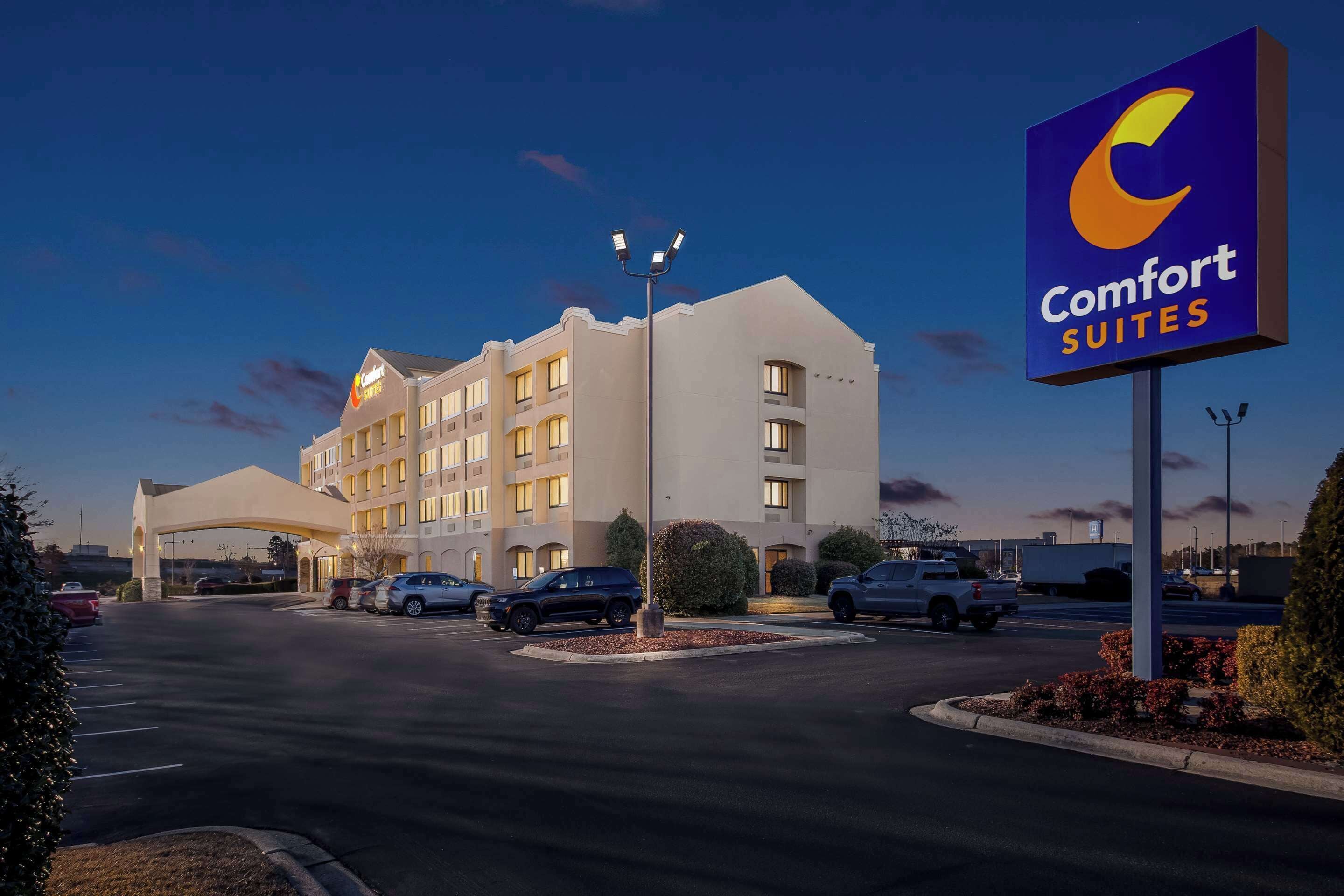 A Comfort Suites hotel with a modern design, a parking lot, and a clear sky.
