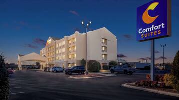 A Comfort Suites hotel with a modern design, a parking lot, and a clear sky.