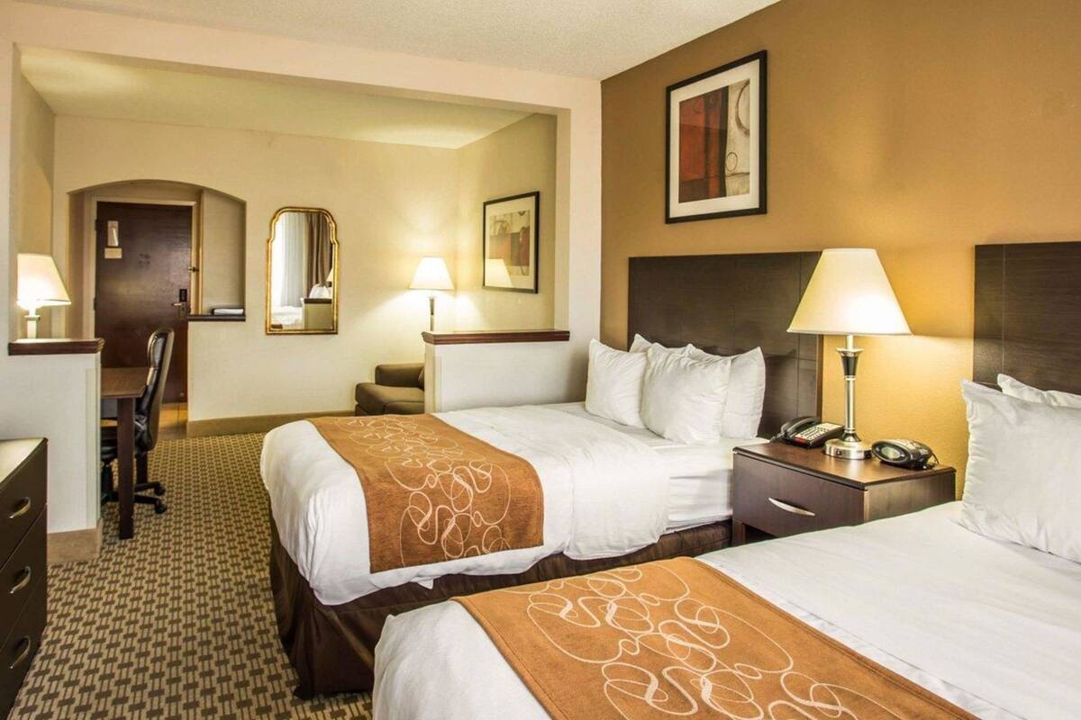Habitación de hotel con dos camas, un escritorio, una silla, un aparador y un espejo.