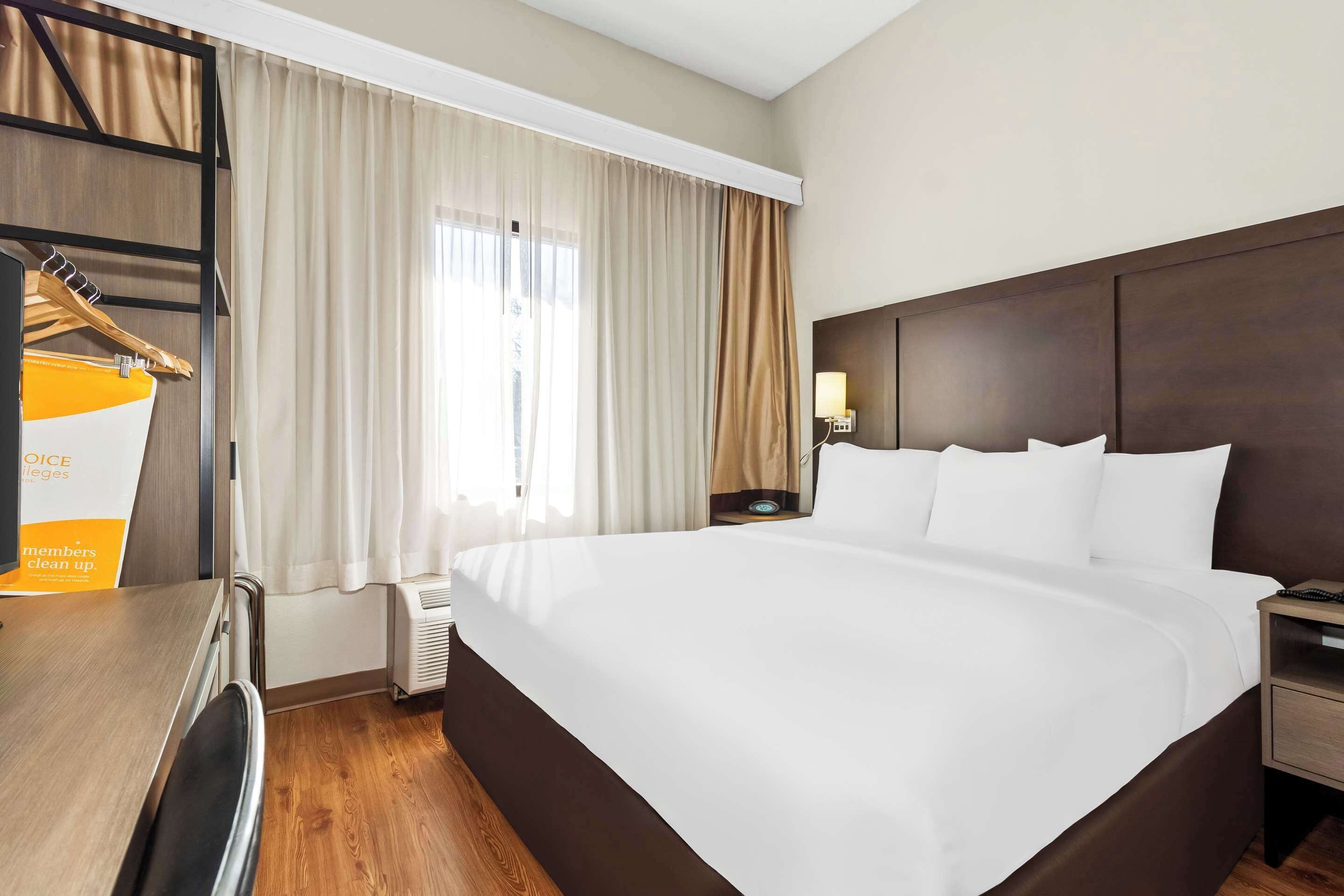 A hotel room with a large bed, a desk with a chair, a wardrobe, and a window with curtains.