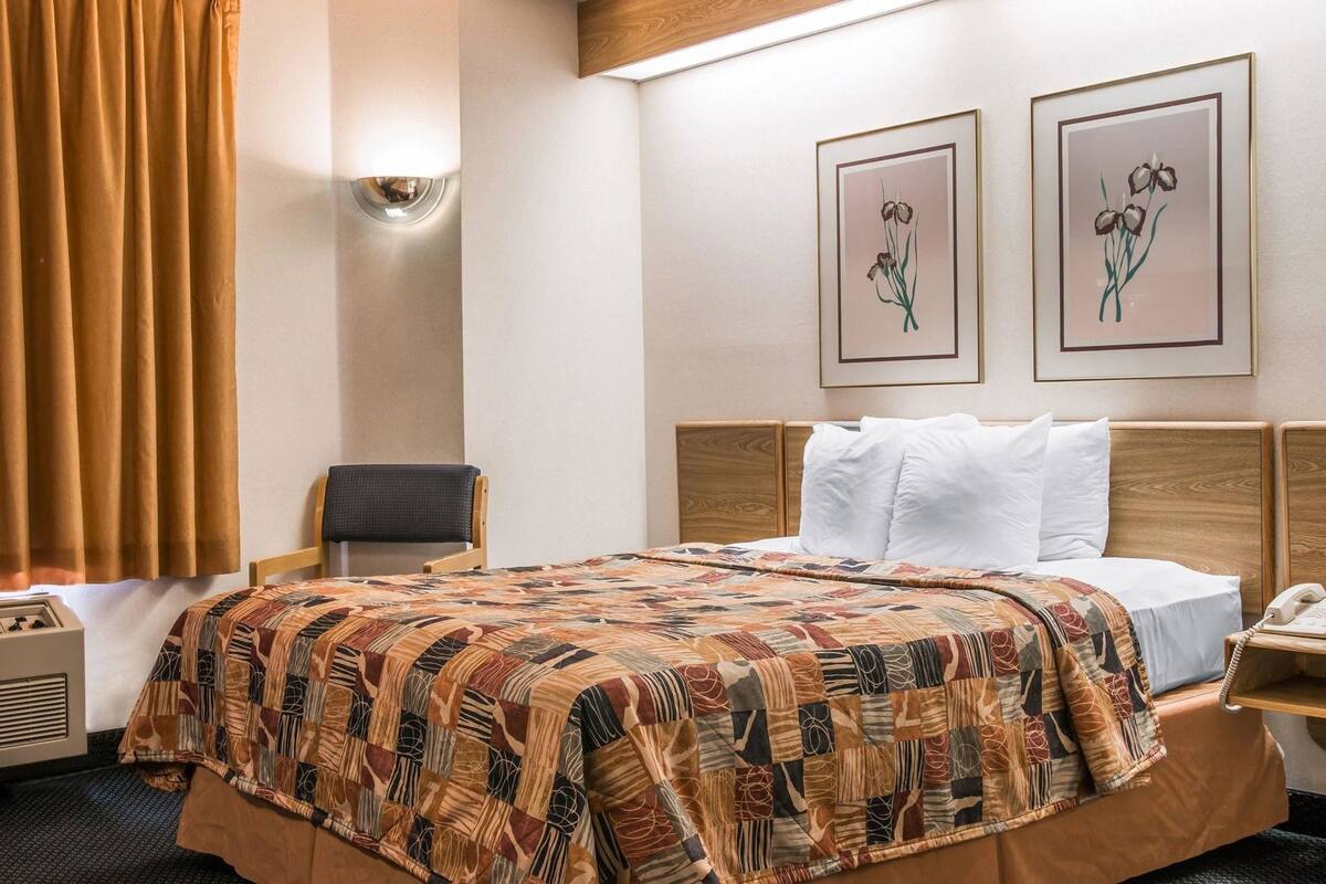 Ein Hotelzimmer mit einem Bett, einem Sessel, einem Nachttisch mit Telefon und zwei gerahmten Blumenbildern an der Wand.