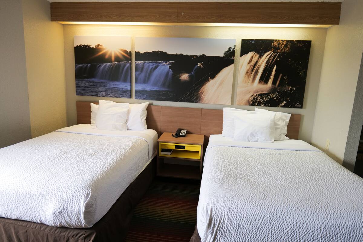 Ein Hotelzimmer mit zwei Betten, einem Holzkopfende, einem Nachttisch mit Telefon und zwei an der Wand befestigten Bildern von Wasserfällen.